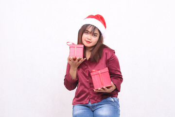 beautiful young asian indonesian girl carrying gift box at christmas santa claus hat modern shiny red shirt outfit looking at camera plain on white background for promotion and advertising