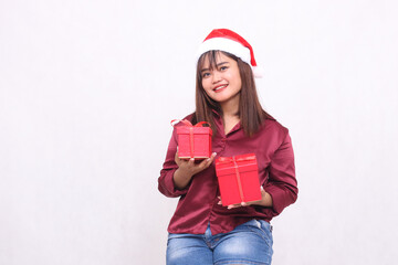 beautiful young asian indonesian girl smiling carrying gift box at christmas santa claus hat modern red shirt outfit lifting box up and down on white background for promotion and advertising