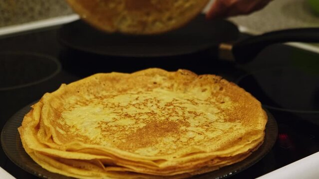 Frying crepes. Making homemade pancakes for family breakfast. Stacking crepe on a plate from a hot pan. Home cooking. Maslenitsa holiday.