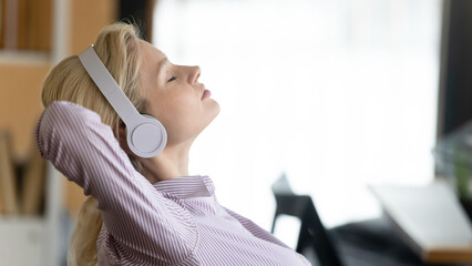 Close up of calm young Caucasian woman in earphones relax listen to music at home on gadget. Happy...
