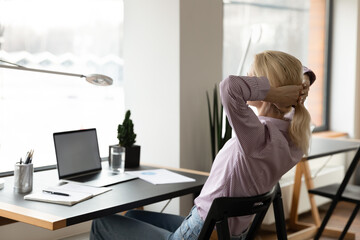 Back view of relaxed young woman rest at desk in home office take nap or sleep at workplace. Calm...