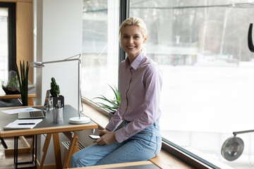 Portrait of smiling young Caucasian female employee pose in modern workplace with smartphone. Happy...