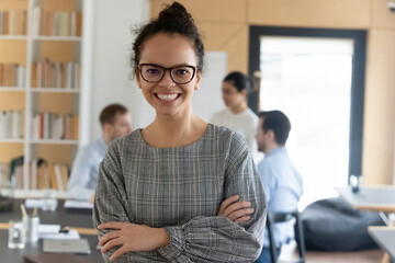 Portrait of smiling millennial 20s African American female employee in glasses pose in modern office. Happy young ethnic businesswoman feel confident successful. Employment, leadership concept.