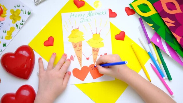 Child making homemade greeting card. little girl making  two ice cream with smile and hearts from paper as gift for Mothers day, Birthday or Valentines day . Arts  crafts concept. Hello summer 