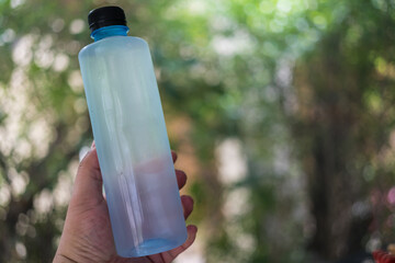 Man hand holding drinking water bottle on blurred green bokeh background