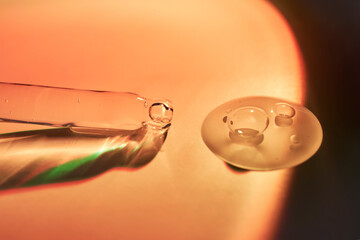 A dropper and a drop of sunscreen body serum in the orange sunset light.