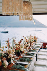 Festive table with bouquets of flowers and candles stands on the pier