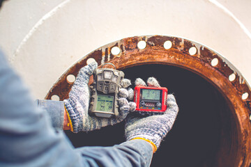 Worker hand holding gas detector inspection safety gas testing at front manhole stainless tank - obrazy, fototapety, plakaty