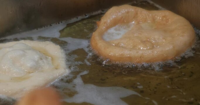 Turkish pisi (deep-fried dough) is cooking in oil in frying pan on the stove
