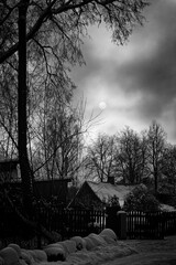 winter landscape in Latvia village. Silhouettes of trees, crooked old houses, sun through dark...