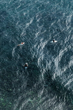 Aerial view of three surfers waiting waves seated in surfboards, textured patterns of the ocean in indonesia, Asia