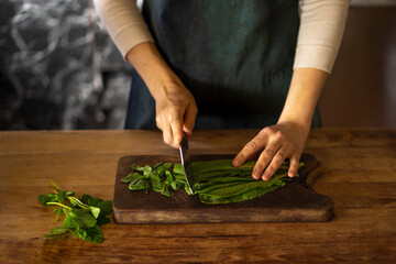 Woman cooking, cutting green salad on wooden table, zoom on hands. High quality photo