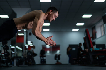 Fototapeta na wymiar Muscular shirtless man doing push-ups in a jump in the gym. 