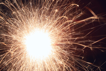 A burning sparkler on a black background with bokeh.