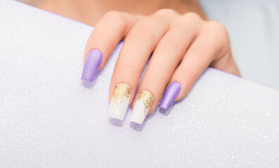Obraz na płótnie Canvas Female hands with long nails with glitter nail polish. Long purple and gold nail design. Women hand with sparkle manicure.