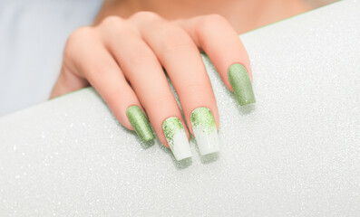 Obraz na płótnie Canvas Female hand with long nails with glitter nail polish. Long green nail design. Women hand with sparkle manicure on glitter background