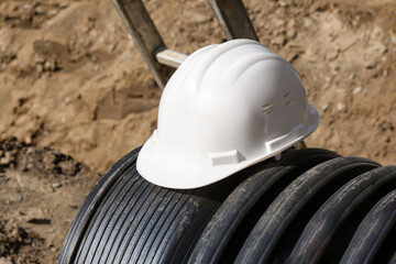Close-up of a white plastic safety helmet on a black corrugated pipe.