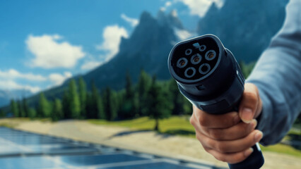Focus EV charger pointing in front of camera with businessman's hand in blurry background with...