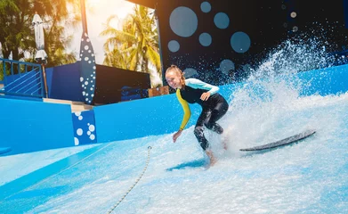 Foto auf Leinwand Beautiful young woman surfing on a wave simulator at a water amusement park © romaset