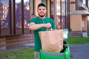 Happy young man courier in green uniform with big thermo bag or backpack deliver food from restaurant or grocery market to home. Food delivery.