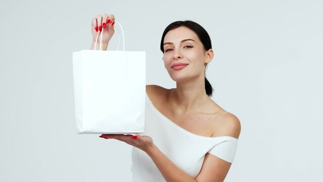 Happy woman with a white bag in her hands on a light background. Charismatic, positive woman enjoying a discount and shopping. Shopping, delivery and gifts concept.