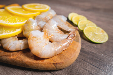 Boiled shrimp in the shell without a head and lemon wedges on a serving wooden plate, close-up of...