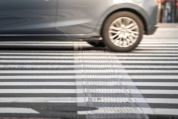 Pedestrain crossing (zebra) line on street in the city with blurred background of a fast car is passing. Transportation scene photo, selective focus on the road surface. 