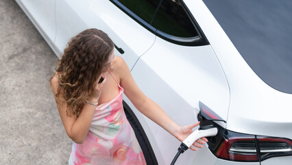Aerial top view eco-friendly woman recharge electric vehicle from EV charging station, using EV...