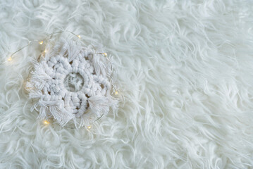 The white snowflake is made in the macrame technique on a white fur background, flat lay,free space. - obrazy, fototapety, plakaty