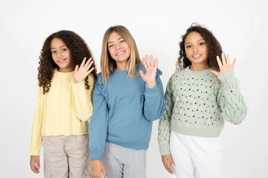 Three beautiful multiracial kid girls  Waiving saying hello happy and smiling, friendly welcome gesture.