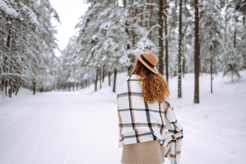 Beautiful woman posing with her back in the winter forest. Great winter weather and atmosphere. She is dressed in a winter coat, hat and scarf. Happy winter time. Christmas.