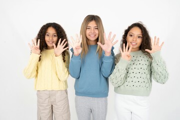 Three beautiful multiracial kid girls  showing and pointing up with fingers number nine while...