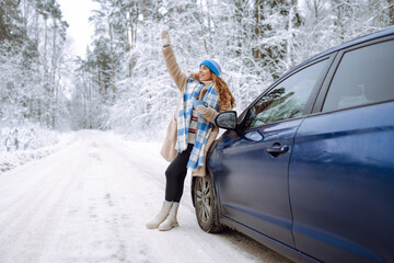 Beautiful young woman near a car in a snowy forest. First snow, great mood.  A traveler poses near a car in nature. Concept of car travel, vacation.