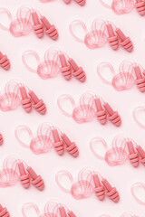 Reusable silicone pale pink color earplugs, for swim, sleep, rest as minimal trend pattern on pink background. Soft, flexible ear plug on cord against noise, protect hear, close up, top view