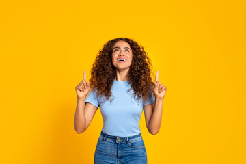 Joyful woman pointing up on a yellow background