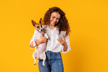 Fototapeta na wymiar Smiling woman and dog with phone on yellow background
