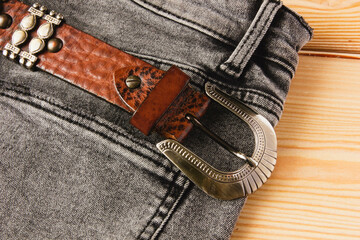 Brown leather belt and gray jeans on wooden background