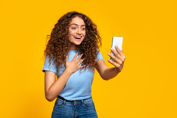 Joyful woman video calling on smartphone on yellow - obrazy, fototapety, plakaty