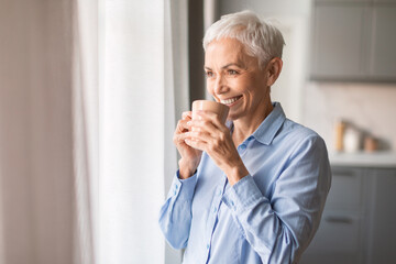 Relaxed smiling mature woman drinking coffee at home