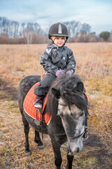Little cute girl riding a little pony in field in the winter