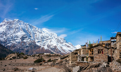 Stone houses with traditional Tibetan flags in a small village nestle at the base of the snow-clad Annapurna range