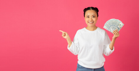 Happy asian woman holding dollar cash and pointing aside at copy space
