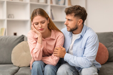 Husband Comforting Supporting Depressed Wife Sitting On Couch At Home - obrazy, fototapety, plakaty