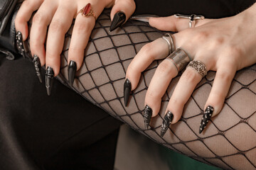 Hands with long black nails and gothic style finger rings lying on leg in fishnet tights