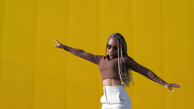 young beautiful woman with a long braids dancing on a yellow background