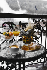 New Year's breakfast on the hotel balcony in the mountains. Coffee with croissant, juice and tangerines against the backdrop of snow-capped mountains. Concept of winter holidays