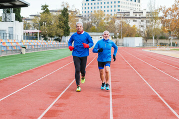 Obraz premium Two elder Caucasian men in sportswear running on an athletic track, focused and fit
