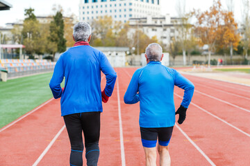 Aged Caucasian runners in blue on red track, ready for training, in sports attire, back view