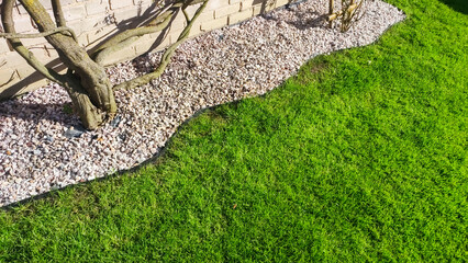  Lush green lawn with an edging of small garden stones - obrazy, fototapety, plakaty