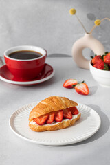 A fresh croissant with ricotta and fresh strawberries. Croissant with black coffee.